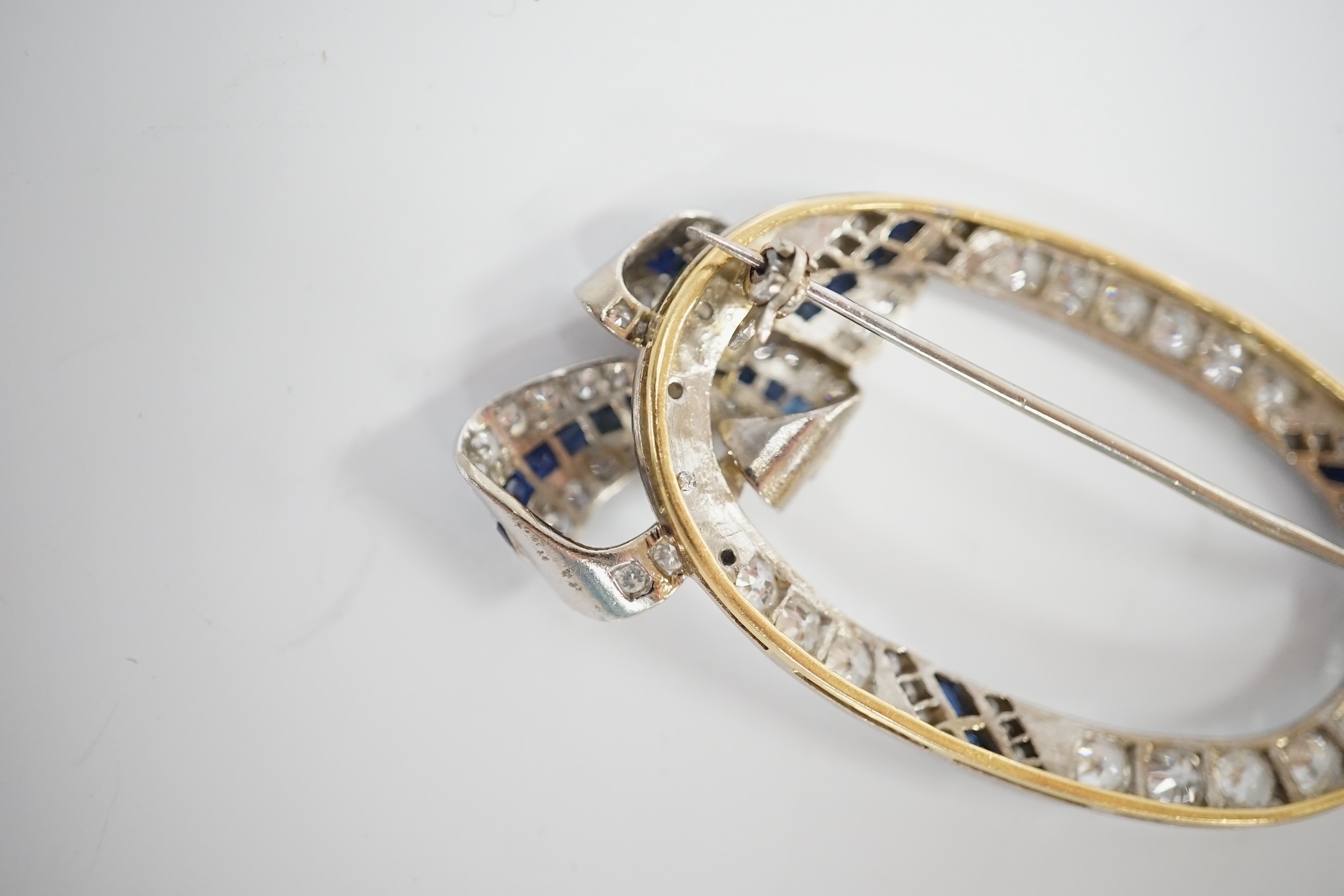 A yellow and white metal, sapphire and millegrain set diamond cluster oval open work brooch, with ribbon bow motif, 50mm, gross weight 11 grams. Condition - good